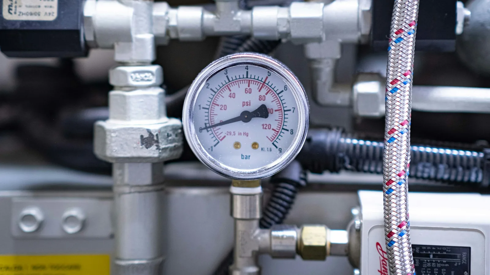 A pressure gauge fitted to supply pipework, reading water pressure in psi
