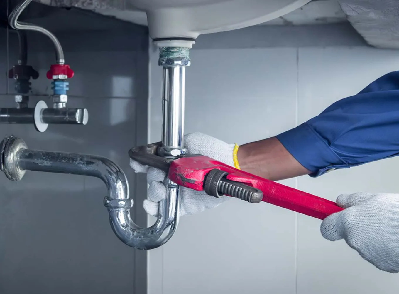 A plumber tightening the P-trap under a sink with a pipe wrench